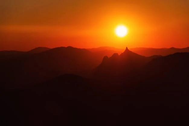 Sun setting behind a silhouetted mountain ridge, glowing orange sky