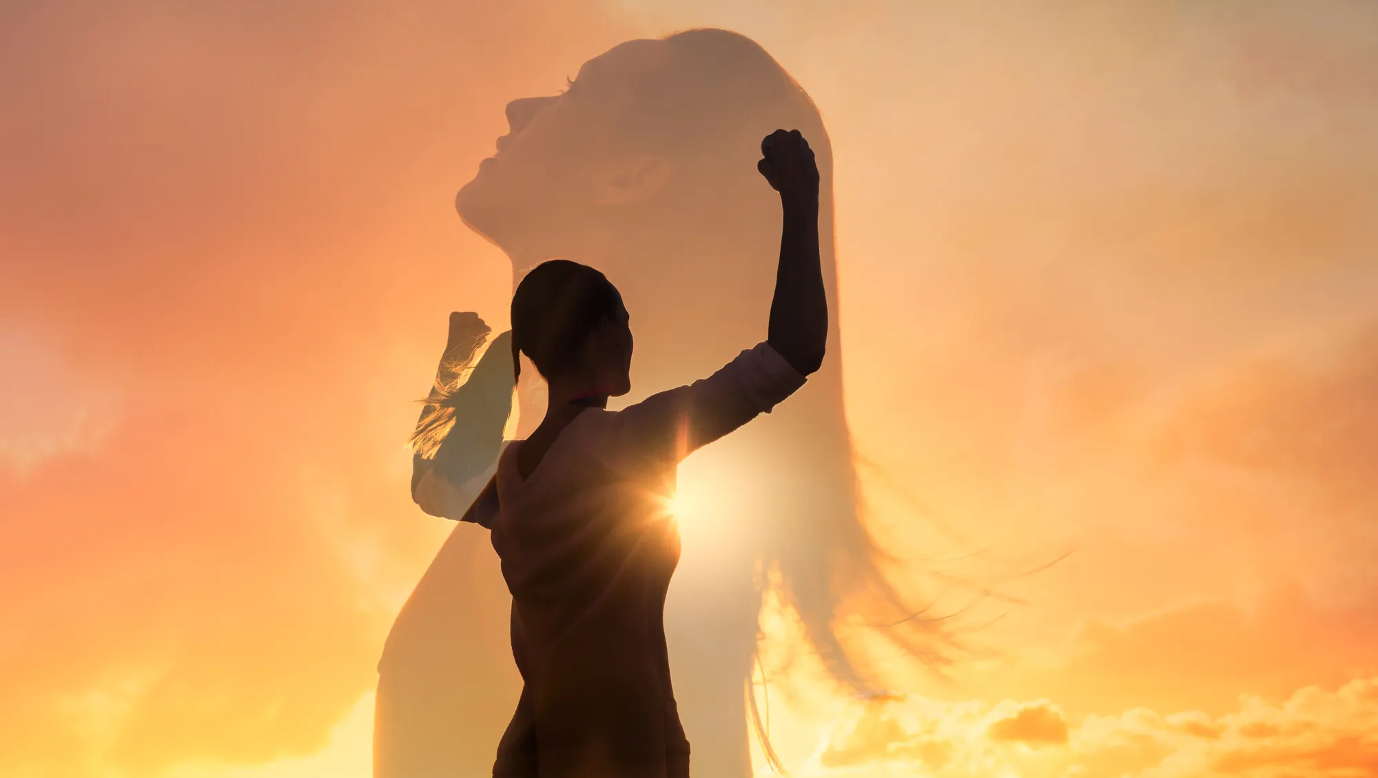 Silhouette of a woman raising her fist in triumph against a sunset sky